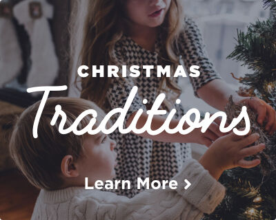 Two young children, filled with joy, decorating a Christmas tree with pine cones. Image links to Christmas Traditions page.